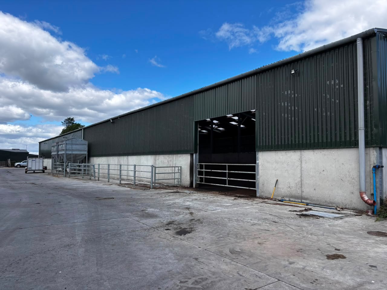 Long green-clad farm building and concrete yard at Mount Congreve Farm under a blue sky